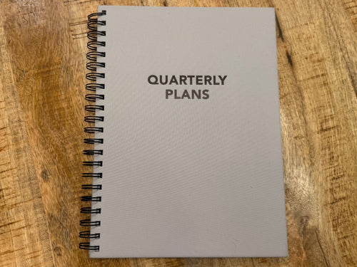 Notebook titled 'Quarterly Plans' on a wooden surface